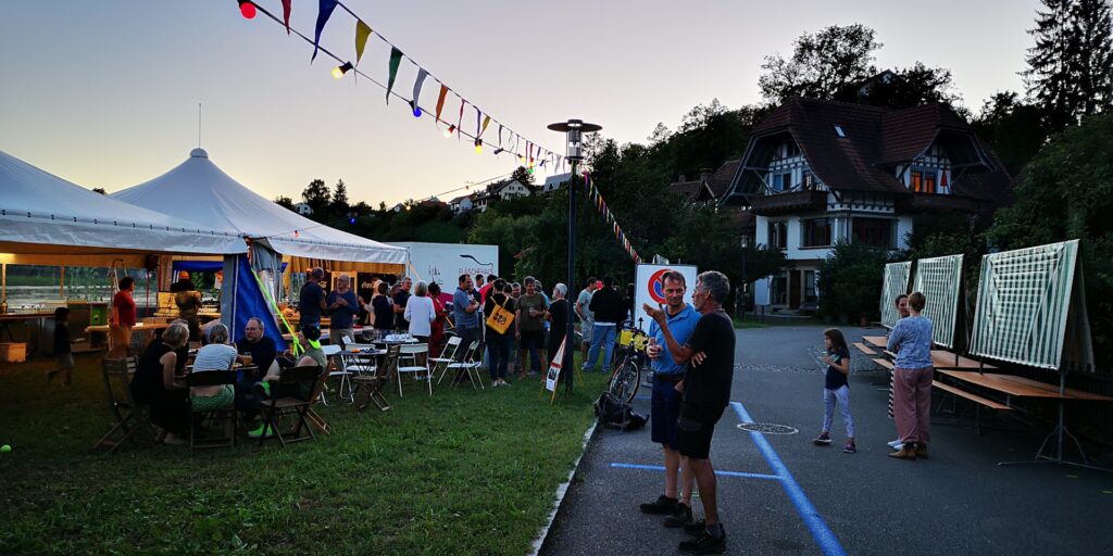 Leute stehen am Neuzuzüger- und Helfer-Apéro vor dem Festzelt und diskutieren miteinander.