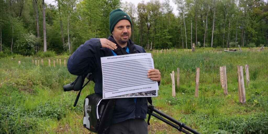 Tom erklärt, dass 650 Lastwagenladungen mit ausgebaggertem Material aus der ehemaligen Deponie fachgerecht auf sicheren Deponien entsorgt werden mussten und illustriert dies, indem er ein Plakat mit 650 Lastwagensymbolen zeigt.