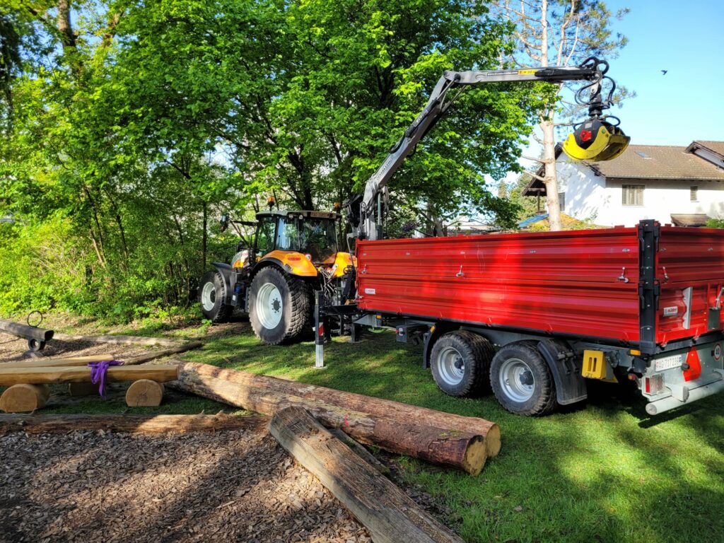 Gelber Traktor mit rotem Anhänger und Kran